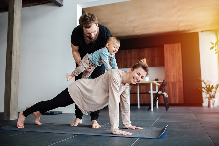 Mother doing plank, father holding their baby on her back,