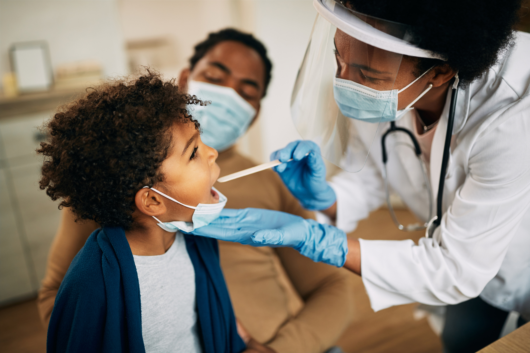 doctor with face mask examining boy's throat during a home visit.